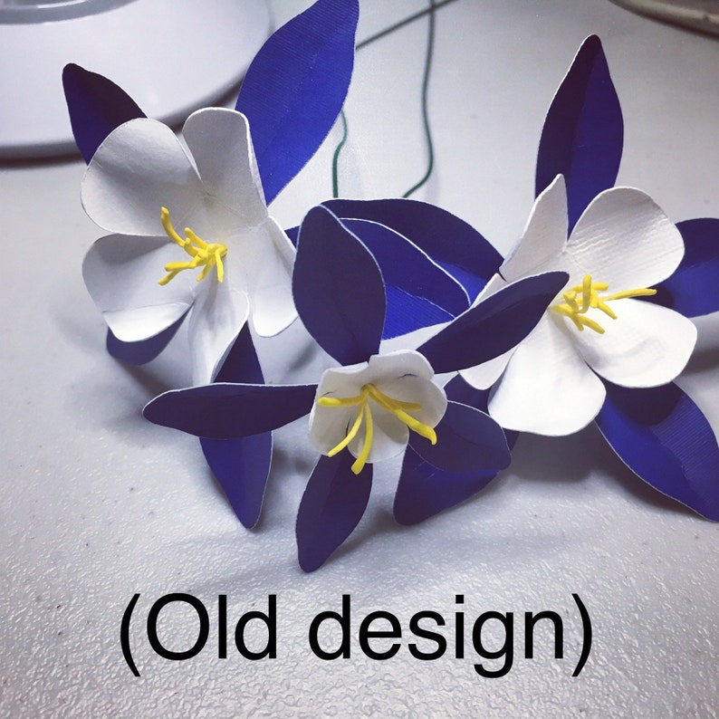 May include: Three white paper flowers with yellow centers and blue paper leaves. The flowers are arranged in a bouquet and the text "(Old design)" is visible below the flowers.