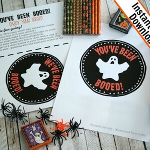 Könnte beinhalten: Druckbarer Halloween-Schild "You've Been Booed!" mit einem Geist und dem Text "We've Been Booed!" in Schwarz und Orange. Das Schild ist auf weißem Hintergrund mit schwarzem und orangefarbenem Rand.