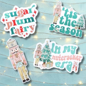 May include: Four Christmas-themed stickers featuring a nutcracker, a Christmas tree, and festive text. The stickers feature a pink and green color scheme with white outlines. The text on the stickers reads "sugar plum fairy", "'tis the season", "in my nutcracker era", and a nutcracker holding a candy cane.
