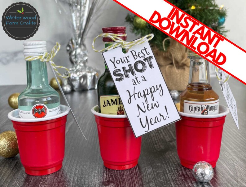 Puede incluir: Tres vasos de pl&aacute;stico rojos con botellas de licor en miniatura en su interior. Cada vaso tiene una etiqueta. La etiqueta del vaso del medio dice "Your Best Shot at a Happy New Year!"