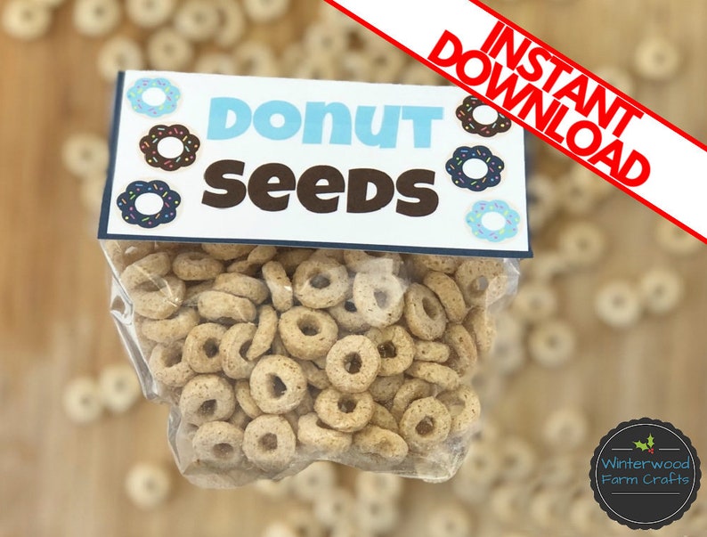 May include: A clear plastic bag filled with donut-shaped cereal. The bag has a blue and white label that says "Donut Seeds" with a donut graphic on each side.