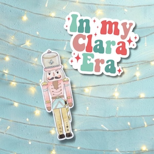 May include: A colorful sticker with the text "In my Clara Era" and a cartoon illustration of a nutcracker in a pink and blue uniform.
