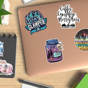 Op de afbeelding: Een verzameling kleurrijke stickers met kampeer- en reisthema's. Ontwerpen omvatten een blauwe en turquoise camper met de tekst "GLAMPER LIFE", een pot met een camper en de tekst "COLLECT MOMENTS", en een ronde sticker met het woord "WANDER".