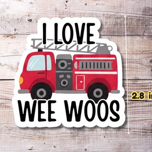 Op de afbeelding: Een sticker met een rode brandweerwagen met de tekst "I LOVE WEE WOOS". De sticker is ongeveer 7,1 cm hoog. De brandweerwagen heeft een ladder bovenop en zwarte wielen.