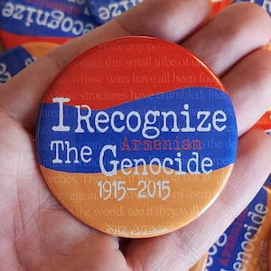 May include: A red, white and blue button with the text "I Recognize The Armenian Genocide 1915-2015" in white lettering. The button is being held in a hand.
