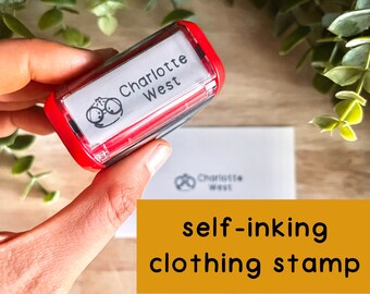 May include: Red self-inking clothing stamp with the name "Charlotte West" and a cartoon image of a person wearing glasses.