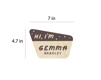 May include: A wooden name tag with the text "Hi, I'm" in a dark brown upper section and "GEMMA BRADLEY" in a lower section. The tag is 7 inches wide and 4.7 inches tall.