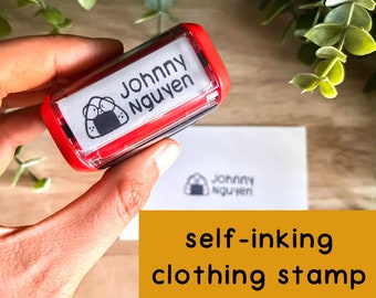 May include: Red self-inking clothing stamp with a cartoon onigiri and the name "Johnny Nguyen" printed on it.