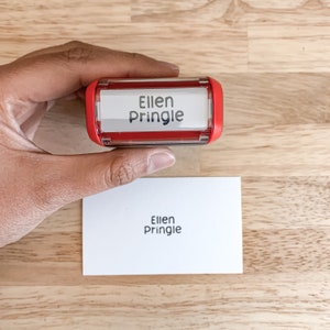 May include: Red self-inking stamp with a clear window displaying the name "Ellen Pringle".