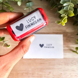 May include: Red self-inking stamp with a white label. The label has a black heart and the text "LUCY FINNEGAN".