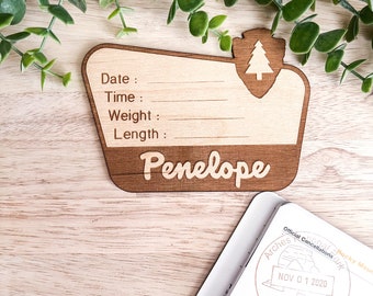 May include: A wooden sign with a brown stain and a light wood finish. The sign is shaped like a park sign and has a small tree icon in the top right corner. The sign has the text "Date:", "Time:", "Weight:", "Length:", and "Penelope" engraved on it.