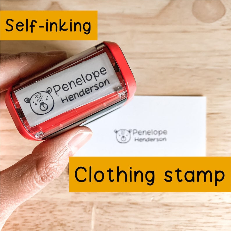Pu&ograve; includere: Timbro per abbigliamento autoinchiostranti rosso con un'etichetta bianca che dice "Penelope Henderson" e una piccola illustrazione di un orso. Il timbro viene utilizzato per creare un'impronta su un cartoncino bianco.