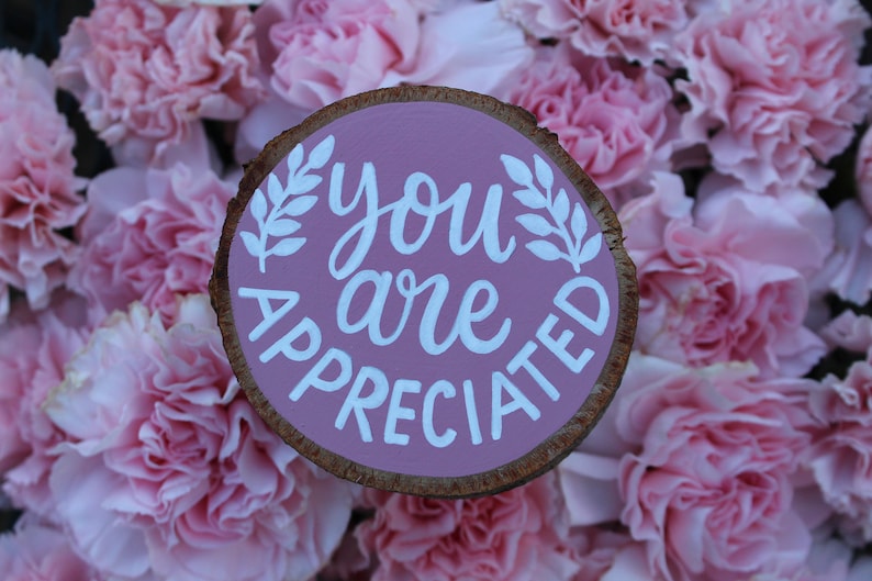 K&ouml;nnte beinhalten: Ein rosafarbenes Holzschild mit den Worten "you are appreciated" in wei&szlig;er Farbe. Das Schild ist von rosa Nelken umgeben.