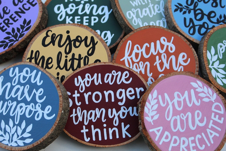K&ouml;nnte beinhalten: Zehn runde Holzscheiben mit bemalten inspirierenden Botschaften. Die Botschaften beinhalten "You have purpose", "You are stronger than you think", "Enjoy the little things", "Focus on the good", "Keep going", "Just be you", "With grateful heart" und mehr.