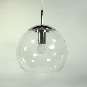 May include: A clear glass pendant light with a spherical shade. The shade has a speckled texture and is suspended from a chrome-colored metal fixture. A light bulb is visible inside the shade.