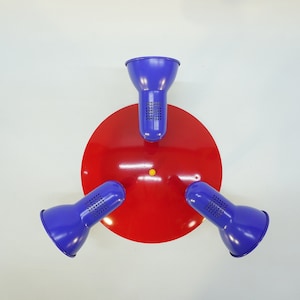 May include: A red circular ceiling fixture with three blue lampshades. The lampshades are angled downwards and have a textured surface.