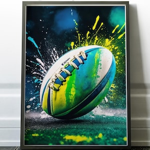 Könnte beinhalten: Gerahmter Kunstdruck mit einem farbenfrohen Rugbyball mit blauen, grünen und gelben Farbspritzern. Der Ball ist weiß mit blauen Schnürsenkeln und einem grün-gelben Design. Der Hintergrund ist dunkel mit Farbspritzern.