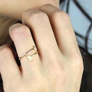 May include: A gold-toned ring with a delicate arrow design. The ring is worn on the index finger of a person's hand.