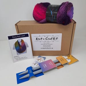May include: A knitting kit for a cowl, featuring a ball of multicoloured yarn, knitting needles, and instructions. The box is labelled "Knit a Cowl Kit". The kit also includes a card with the text "Easy knit cowl". The needles are 25 cm long.