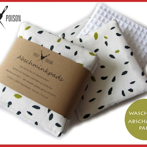 Op de afbeelding: Set van vier witte katoenen make-up remover pads met een zwart en groen bladpatroon. De pads zijn verpakt met een bruin papieren label waarop "Abschminkpads" staat en wasinstructies staan. Het label vermeldt ook "4 Stück / 100% Baumwolle / 9,5 cm x 9,5 cm".
