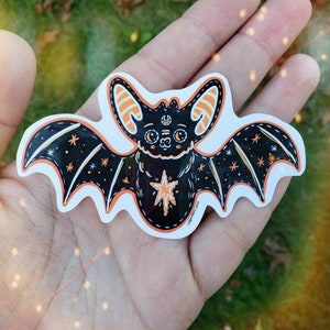 May include: A black and orange bat sticker with a star and moon design. The bat has a stitched outline and a cute, cartoon-like face. The sticker says "Legendairy Llama" at the bottom.