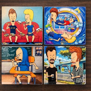 Puede incluir: Juego de cuatro posavasos cuadrados de cerámica con personajes de dibujos animados en varias escenas. Un posavasos muestra dos personajes en un sofá rojo, otro los representa en una lavadora, y los otros los muestran en diferentes entornos.
