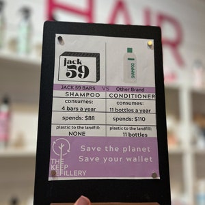 Puede incluir: Un letrero negro de pizarra con una comparaci&oacute;n entre las barras de champ&uacute; y el champ&uacute; l&iacute;quido. El letrero dice "Jack 59 Bars" y "Otra marca". El letrero tambi&eacute;n incluye el texto "Salva el planeta, Salva tu cartera".