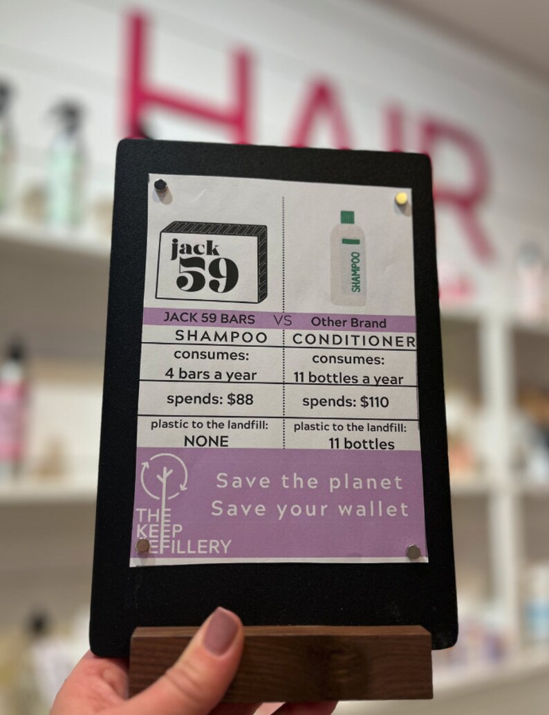 Puede incluir: Un letrero negro de pizarra con una comparaci&oacute;n entre las barras de champ&uacute; y el champ&uacute; l&iacute;quido. El letrero dice "Jack 59 Bars" y "Otra marca". El letrero tambi&eacute;n incluye el texto "Salva el planeta, Salva tu cartera".