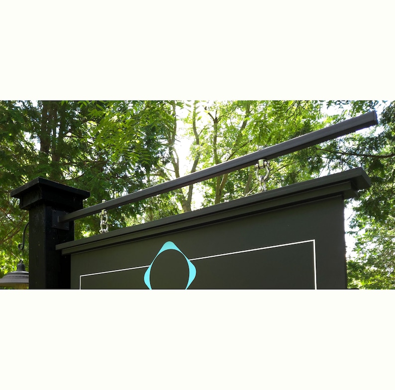May include: A black sign with a teal logo is hanging from a black metal bar. The sign is attached to a black post.