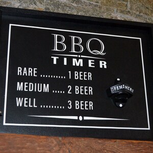 May include: Black framed sign with white text that reads "BBQ TIMER" and a list of doneness levels for meat with corresponding beer counts. The sign has a bottle opener attached.
