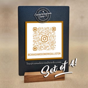 Puede incluir: Un letrero negro de pizarra con un c&oacute;digo QR dorado y el texto "@CANADAWOODWORKSALLISTON" y "lisa@canadawoodworks.com". El letrero est&aacute; sobre un soporte de madera y tiene el texto "Set of 4!" escrito en cursiva blanca.