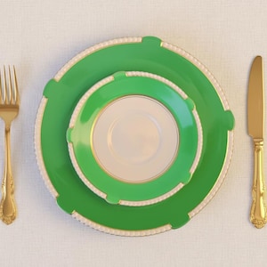 Può includere: Un set di tre piatti in porcellana verde e bianca con finiture dorate, una forchetta dorata e un coltello dorato disposti su una tovaglia bianca. I piatti sono nidificati, con il piatto più piccolo al centro.
