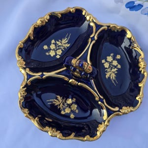 May include: A three-sectioned, navy blue ceramic serving dish with a gold scalloped edge. Each section features a gold floral design. A small, ornate blue and gold handle is attached to the center.