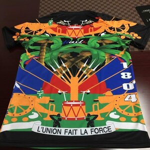 May include: Black t-shirt with a colorful design featuring a coat of arms with palm trees, cannons, drums, and the text "L'UNION FAIT LA FORCE".