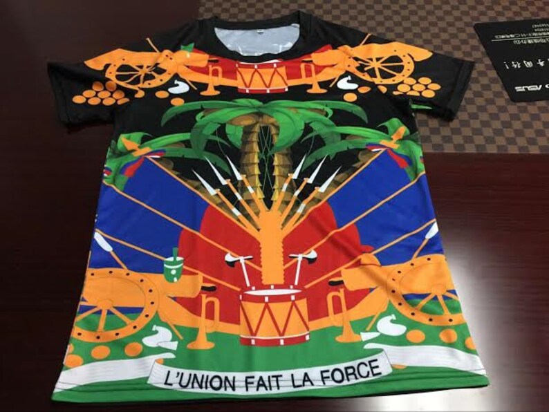 May include: A black short-sleeved t-shirt with a colorful design featuring a flag with cannons, palm trees, and the text "L'UNION FAIT LA FORCE".
