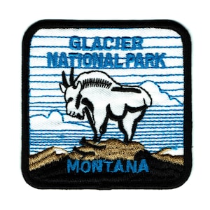 May include: An embroidered patch featuring a white mountain goat standing on a mountain peak. The patch has a blue and white striped background with the text "Glacier National Park Montana" in blue.