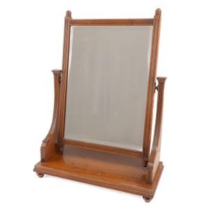 May include: A wooden vanity mirror with a rectangular frame and a tilting design. The mirror is set on a wooden base with decorative detailing. The wood has a warm, natural tone, and the mirror is set against a white background.