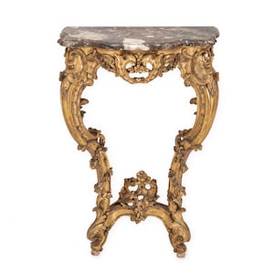 May include: A gold-colored, ornate console table with a marble top. The table features intricate carvings and a curved design. The marble top has a mix of gray, brown, and white tones. The table's legs are also intricately carved.