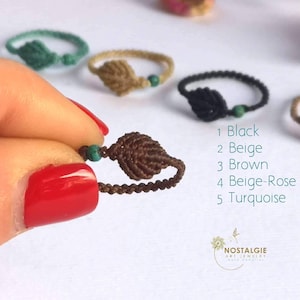 Puede incluir: Cinco pulseras de amistad hechas a mano con cuentas turquesas. Las pulseras están hechas de hilo marrón, beige, negro y turquesa. Las pulseras están dispuestas en una fila, con la pulsera turquesa al final. El texto "1 Negro, 2 Beige, 3 Marrón, 4 Beige-Rose, 5 Turquesa" está escrito debajo de las pulseras.