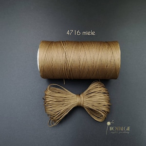 Könnte beinhalten: Eine Spule braunes gewachstes Kordel mit dem Text "47 16 miele" auf schwarzem Hintergrund.