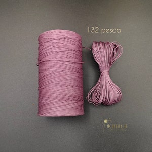 Puede incluir: Una bobina de cordón de color malva con un pequeño trozo del mismo cordón atado en un lazo. El texto "132 pesca" está impreso sobre un fondo blanco.