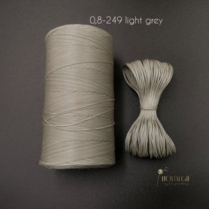 Puede incluir: Una bobina de cordón encerado gris claro, 0,8-249, con una pequeña muestra de cordón atado en un lazo.