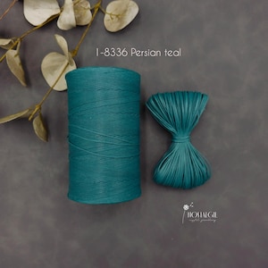 May include: Two spools of Persian teal colored thread. One spool is a tightly wound cylinder, and the other is a bundle of loose threads. The text "1-8336 Persian teal" is above the spools. The background is a dark gray.