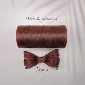 May include: A spool of brown waxed thread labeled "0,6-206 tabacco" sits above a tied bundle of the same thread. The thread is a rich, dark brown color. The bottom bundle is tied in a bow shape. The word "NOSTALGIE" is printed at the bottom.