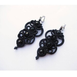 May include: A pair of black earrings with intricate knotted designs and black crystal beads. The earrings are made with black thread and have a silver hook fastening.