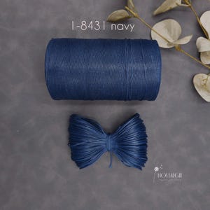 May include: A navy blue spool of twine and a navy blue bow made of twine are displayed on a gray surface. The text "1-8431 navy" is visible at the top. The bow is made of the same material as the spool.