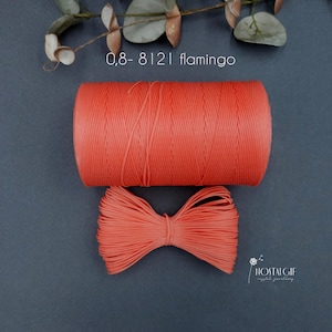 May include: A spool of coral-colored thread and a tied bundle of the same thread are displayed against a dark gray background. The text "0,8-8121 flamingo" is above the spool. The image also includes a sprig of greenery and the "HOSTALGIF crystal jewellery" logo.