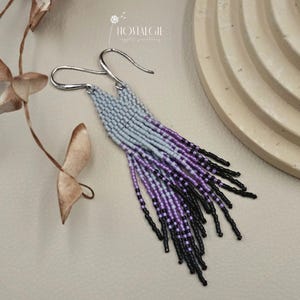 Könnte beinhalten: Ein Paar lange, geperlte Ohrringe mit einem Farbverlauf aus hellblauen, violetten und schwarzen Perlen. Die Ohrringe sind mit silbernen Haken gefertigt.
