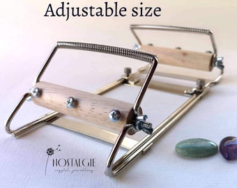 May include: Adjustable metal frame with two wooden rollers, used for wrapping wire around stones. The frame is silver and the rollers are light brown. The text "Adjustable size" is visible above the frame. Two green and purple stones are visible in the foreground.