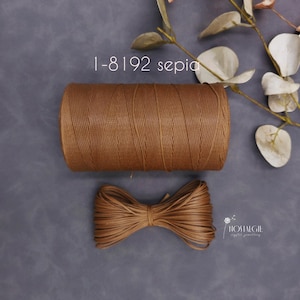 May include: A spool of brown twine and a tied bundle of the same twine are displayed on a gray surface. The text "1-8192 sepia" is visible. Decorative leaves are in the background. The twine is likely used for crafting or packaging.